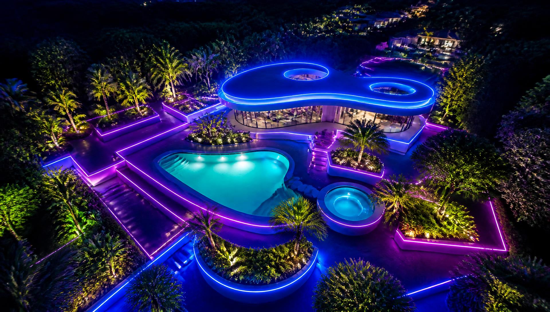 An aerial night view of a futuristic garden layout with glowing geometric paths, an illuminated pool and lit hedges. Images and Photos created by www.house-and-garden-designs.com